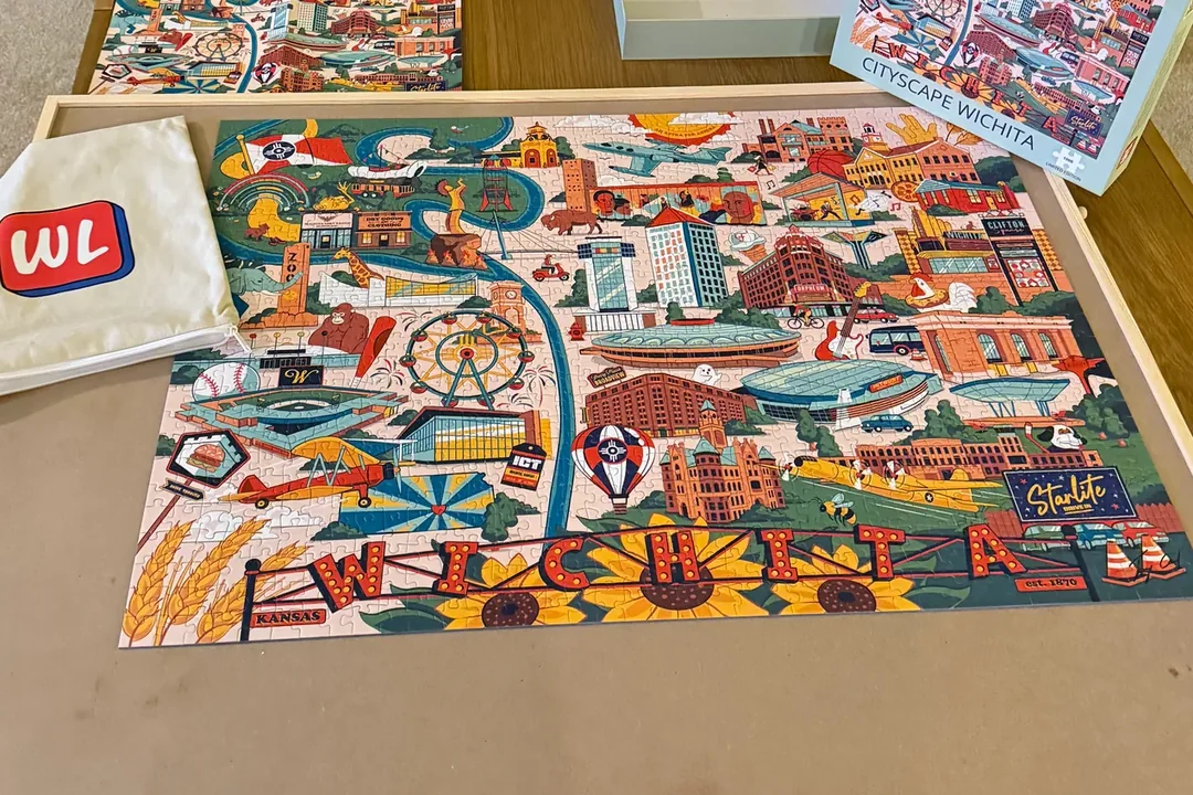 The Cityscape Wichita jigsaw completed on a puzzle board, with the box and a Wichita Life bag
